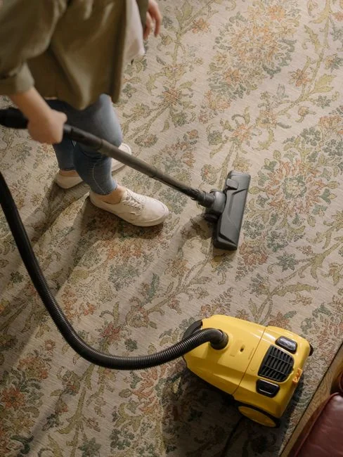 Close-up of people cleaning wooden floor with broom and dustpan indoors.